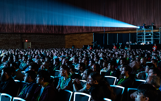 SIGGRAPH attendees sit in a theater, facing a screen, and a projector shines from the back.