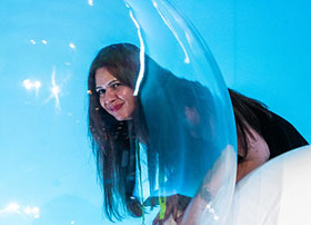 SIGGRAPH attendee smiles through a bubble-like structure in front of a bright blue background.